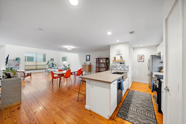 1821 Tuam St, Houston, TX 77004 - kitchen with a peninsula, light wood-style flooring, appliances with stainless steel finishes, white cabinetry, and a kitchen breakfast bar