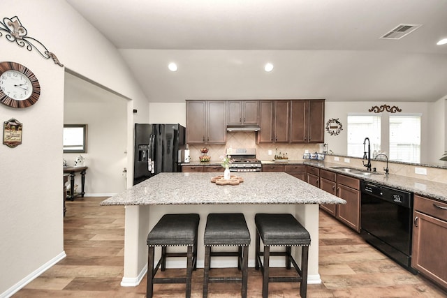 32726 Timber Point Dr, Brookshire, TX 77423 - kitchen featuring black appliances, vaulted ceiling, a breakfast bar area, tasteful backsplash, and under cabinet range hood