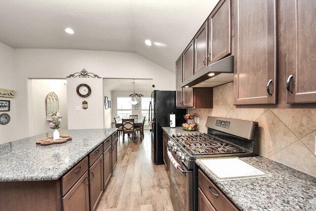 32726 Timber Point Dr, Brookshire, TX 77423 - kitchen with stainless steel range with gas stovetop, under cabinet range hood, a center island, light stone counters, and vaulted ceiling