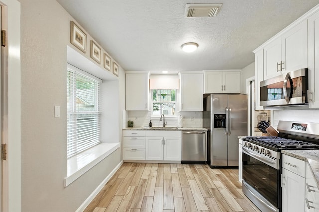 79 Fallshire Dr, The Woodlands, TX 77381 - kitchen featuring stainless steel appliances, light wood-style flooring, tasteful backsplash, plenty of natural light, and a textured ceiling