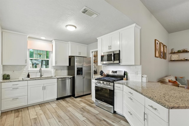 79 Fallshire Dr, The Woodlands, TX 77381 - kitchen featuring stainless steel appliances, a peninsula, white cabinetry, backsplash, and a textured ceiling