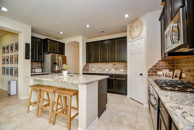 29011 Oldfield Ct, Katy, TX 77494 - kitchen featuring appliances with stainless steel finishes, backsplash, a center island, light stone countertops, and a kitchen bar