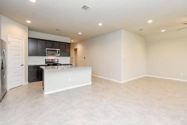 5602 Cedar Crescent Ct, Richmond, TX 77407 - kitchen with stainless steel appliances, tasteful backsplash, a center island with sink, light stone counters, and recessed lighting