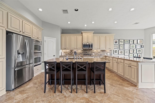 27410 Villa Mountain Ct, Fulshear, TX 77441 - kitchen with cream cabinets, stainless steel appliances, a kitchen island with sink, backsplash, and light stone counters