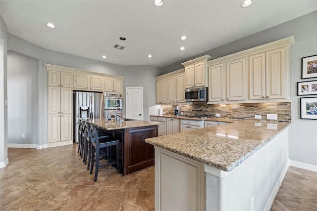 27410 Villa Mountain Ct, Fulshear, TX 77441 - kitchen with cream cabinets, appliances with stainless steel finishes, a breakfast bar, light stone counters, and recessed lighting
