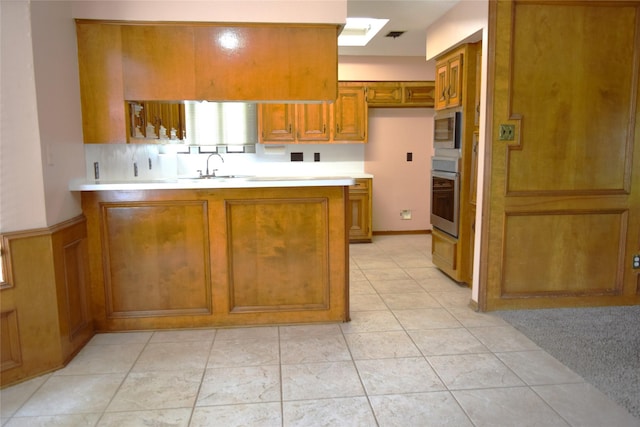 7331 Rancho Mission Dr, Houston, TX 77083 - kitchen featuring stainless steel appliances, brown cabinets, a peninsula, light countertops, and a skylight