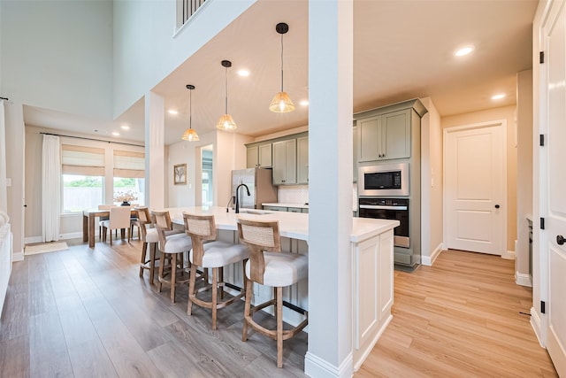 21031 Secretariat Meadow Ln, Tomball, TX 77377 - kitchen with appliances with stainless steel finishes, gray cabinetry, light wood-style floors, light countertops, and a kitchen breakfast bar