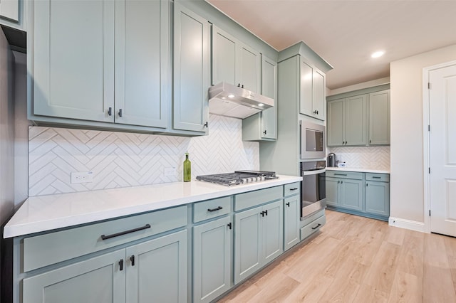 21031 Secretariat Meadow Ln, Tomball, TX 77377 - kitchen featuring appliances with stainless steel finishes, under cabinet range hood, light wood-style flooring, decorative backsplash, and light countertops