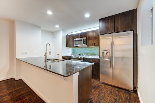 2902 Commerce St, Houston, TX 77003 - kitchen featuring appliances with stainless steel finishes, dark wood-style flooring, dark brown cabinetry, a peninsula, and dark stone counters
