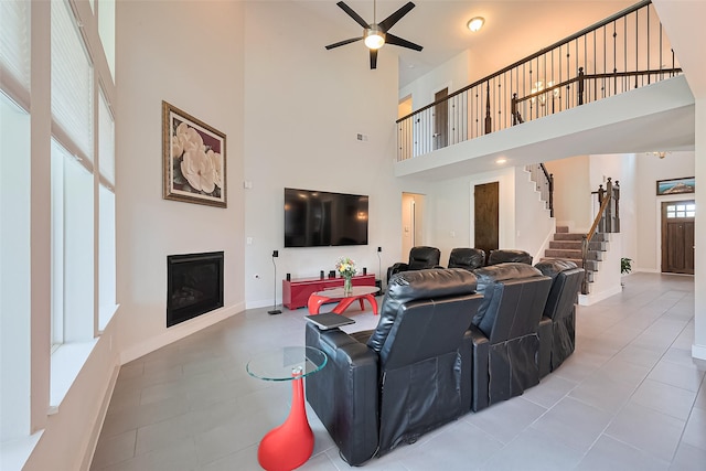 18806 Dove Creek Springs Trl, Cypress, TX 77433 - living room with a high ceiling, a ceiling fan, a glass covered fireplace, tile patterned flooring, and stairs