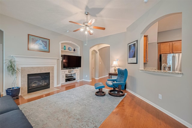 8812 Snowy Owl Loop, Missouri City, TX 77459 - unfurnished living room featuring a ceiling fan, built in shelves, wood finished floors, arched walkways, and a high end fireplace