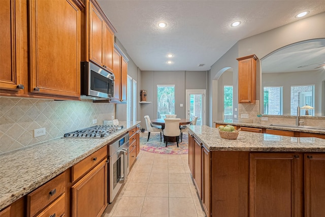8812 Snowy Owl Loop, Missouri City, TX 77459 - kitchen featuring stainless steel appliances, brown cabinets, arched walkways, tasteful backsplash, and light tile patterned floors
