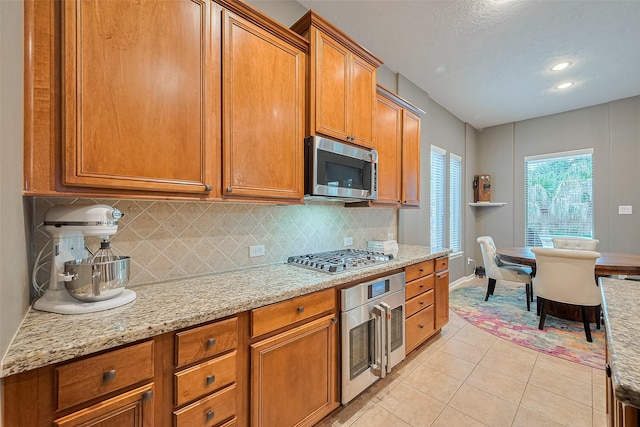 8812 Snowy Owl Loop, Missouri City, TX 77459 - kitchen featuring stainless steel appliances, brown cabinets, light tile patterned flooring, decorative backsplash, and recessed lighting