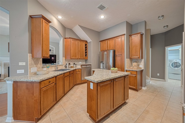 8812 Snowy Owl Loop, Missouri City, TX 77459 - kitchen with stainless steel appliances, washer / clothes dryer, a kitchen island, backsplash, and light tile patterned floors