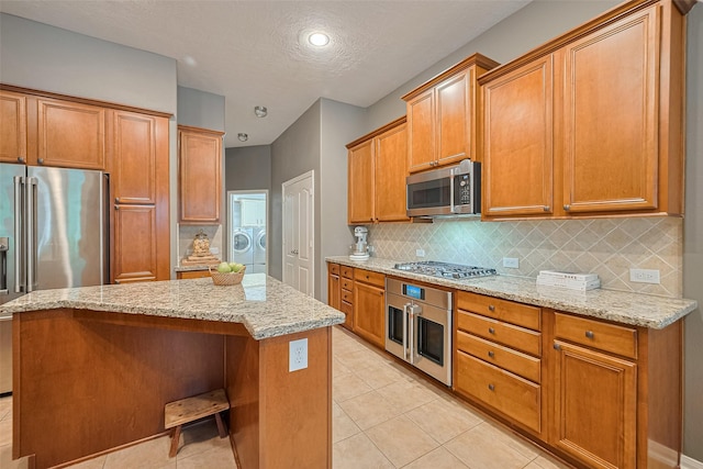 8812 Snowy Owl Loop, Missouri City, TX 77459 - kitchen featuring stainless steel appliances, tasteful backsplash, light stone counters, a kitchen island, and washer and dryer