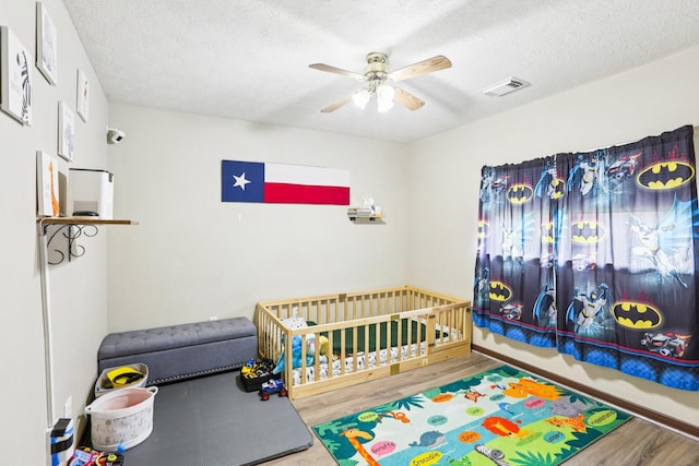 3211 Waterglen Ct, League City, TX 77573 - bedroom featuring wood finished floors, a nursery area, a textured ceiling, and ceiling fan