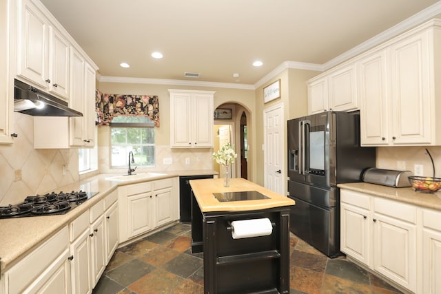 14310 Saint Pierre Ln, Cypress, TX 77429 - kitchen with stainless steel fridge with ice dispenser, under cabinet range hood, black gas cooktop, arched walkways, and stone tile floors