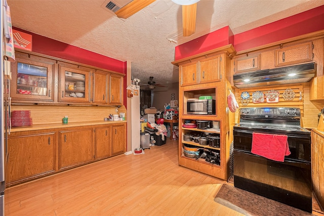 16318 Spinnaker Dr, Crosby, TX 77532 - kitchen with black range with electric stovetop, under cabinet range hood, stainless steel microwave, light wood-style flooring, and brown cabinets