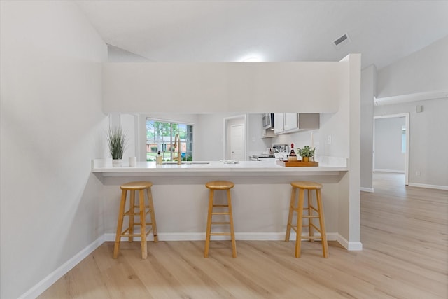 4519 Pineville Ln, Spring, TX 77388 - kitchen with stove, light wood-type flooring, stainless steel microwave, a breakfast bar area, and vaulted ceiling