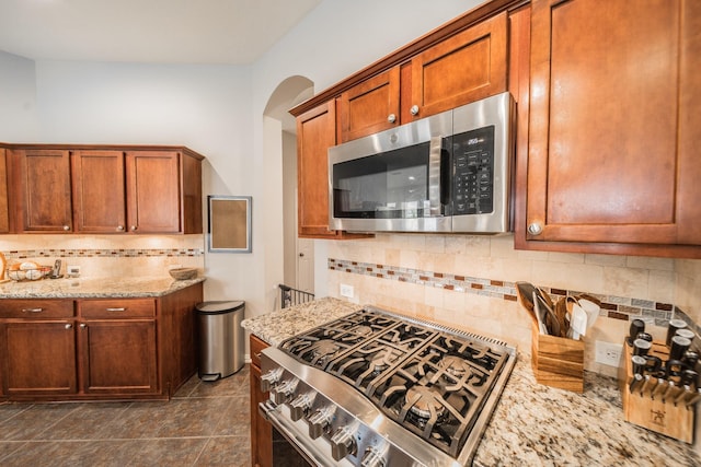 18403 Sierra Falls Ct, Tomball, TX 77377 - kitchen featuring appliances with stainless steel finishes, tasteful backsplash, light stone countertops, arched walkways, and brown cabinets