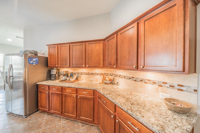 18403 Sierra Falls Ct, Tomball, TX 77377 - kitchen with stainless steel refrigerator with ice dispenser, brown cabinetry, tasteful backsplash, and light stone countertops