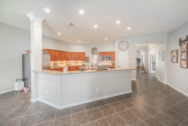 18403 Sierra Falls Ct, Tomball, TX 77377 - kitchen with stainless steel microwave, brown cabinets, arched walkways, recessed lighting, and decorative backsplash