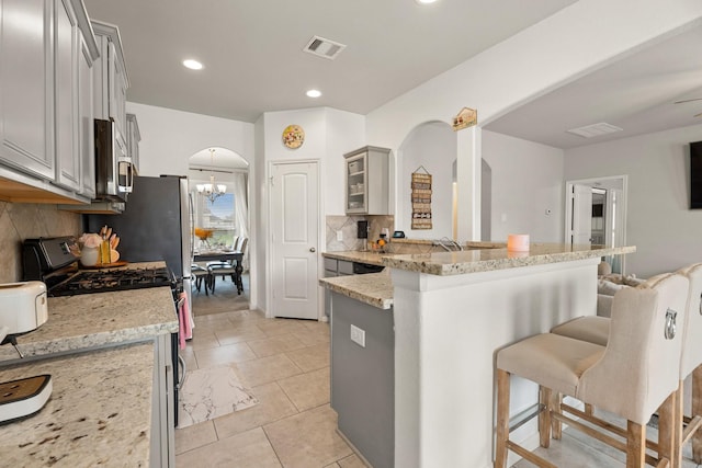 4738 Alluvial Cir, Alvin, TX 77511 - kitchen with a breakfast bar, range with gas stovetop, tasteful backsplash, arched walkways, and light stone counters