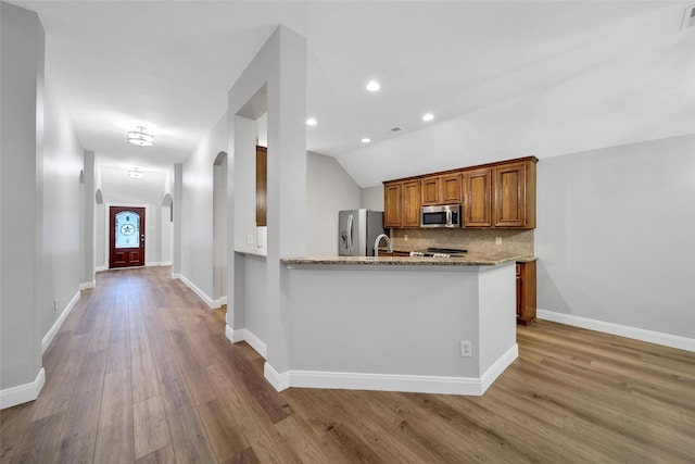 28006 Brendon Trail Ct, Spring, TX 77386 - kitchen featuring stainless steel appliances, arched walkways, tasteful backsplash, wood finished floors, and brown cabinetry