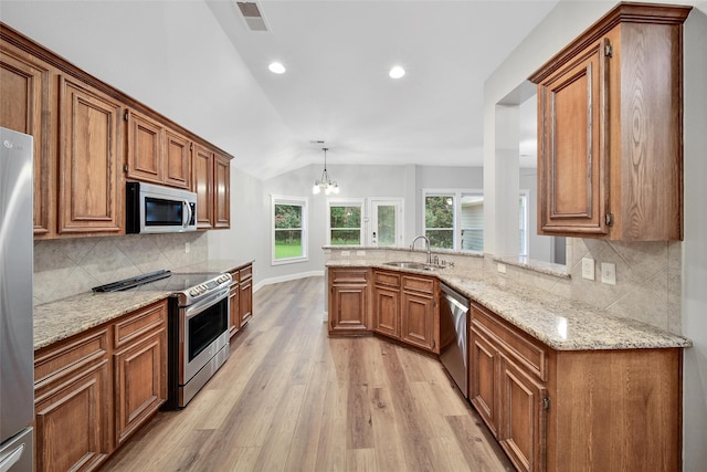 28006 Brendon Trail Ct, Spring, TX 77386 - kitchen with stainless steel appliances, vaulted ceiling, light wood finished floors, brown cabinetry, and light stone counters