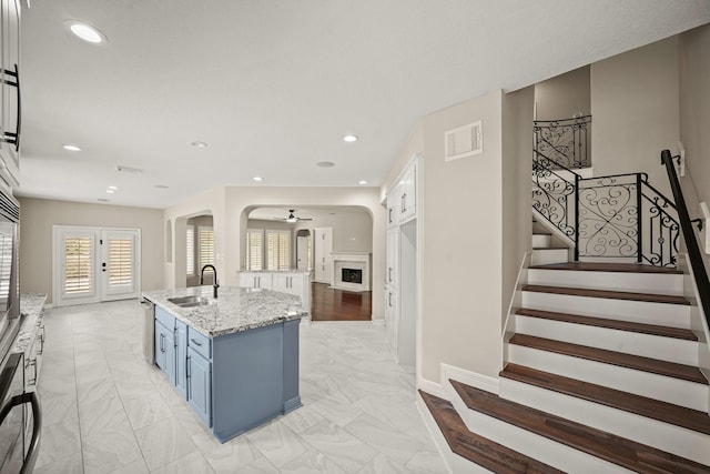 22419 Rippling Shore Ct, Katy, TX 77494 - kitchen featuring blue cabinets, light marble finish flooring, recessed lighting, light stone counters, and an island with sink