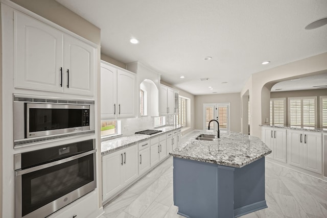 22419 Rippling Shore Ct, Katy, TX 77494 - kitchen featuring appliances with stainless steel finishes, light marble finish floors, light stone countertops, white cabinetry, and an island with sink