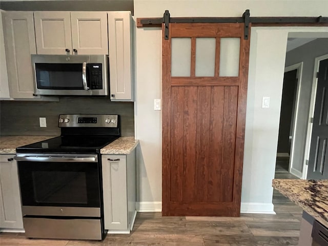 126 2nd Ave, Onalaska, TX 77360 - kitchen featuring appliances with stainless steel finishes, wood finished floors, a barn door, light stone counters, and white cabinetry
