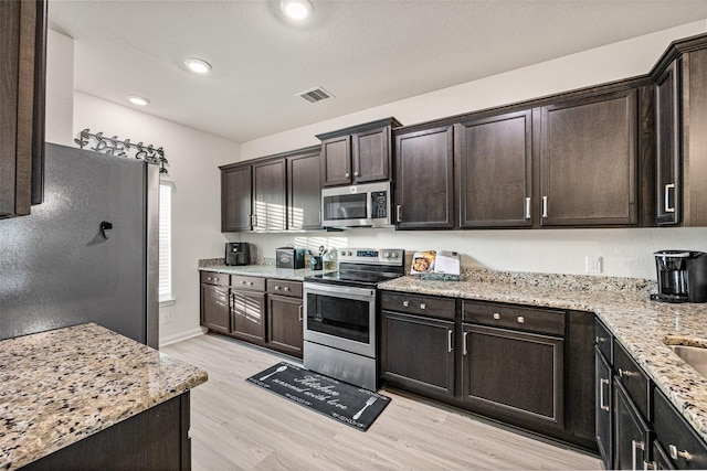 11034 Hillside Creek Dr, Humble, TX 77396 - kitchen featuring appliances with stainless steel finishes, light wood-type flooring, dark brown cabinets, light stone counters, and recessed lighting