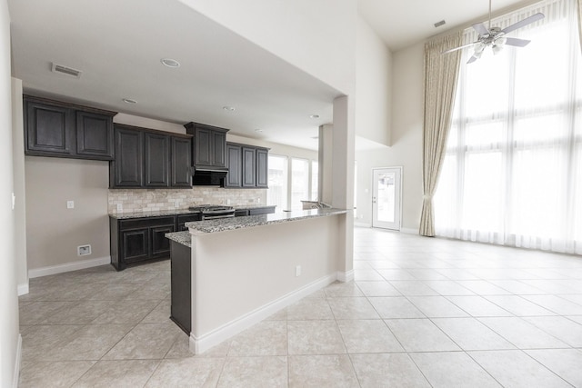 2131 Blossomcrown Dr, Katy, TX 77494 - kitchen featuring light tile patterned flooring, gas stove, light stone countertops, backsplash, and a high ceiling