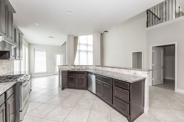 2131 Blossomcrown Dr, Katy, TX 77494 - kitchen featuring appliances with stainless steel finishes, light tile patterned floors, backsplash, dark brown cabinetry, and light stone countertops