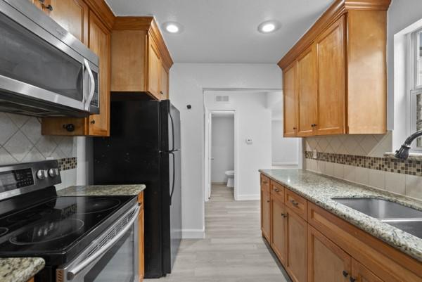 9005 Imogene St Unit C, Houston, TX 77036 - kitchen featuring appliances with stainless steel finishes, backsplash, light wood finished floors, brown cabinetry, and light stone countertops