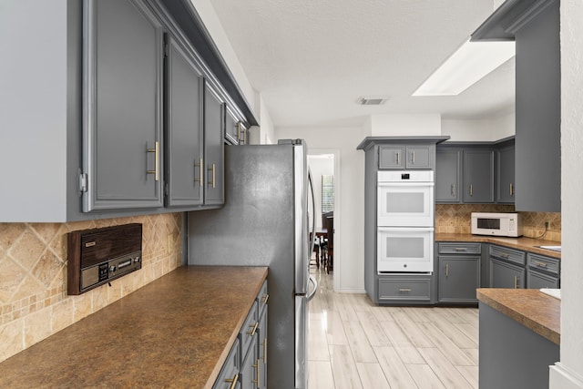 2811 Blue Glen Ln, Houston, TX 77073 - kitchen featuring white appliances, dark countertops, decorative backsplash, gray cabinetry, and light wood finished floors