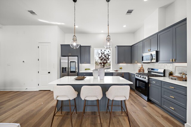 835E Elkhart St, Houston, TX 77091 - kitchen featuring appliances with stainless steel finishes, tasteful backsplash, a breakfast bar area, wood finished floors, and recessed lighting