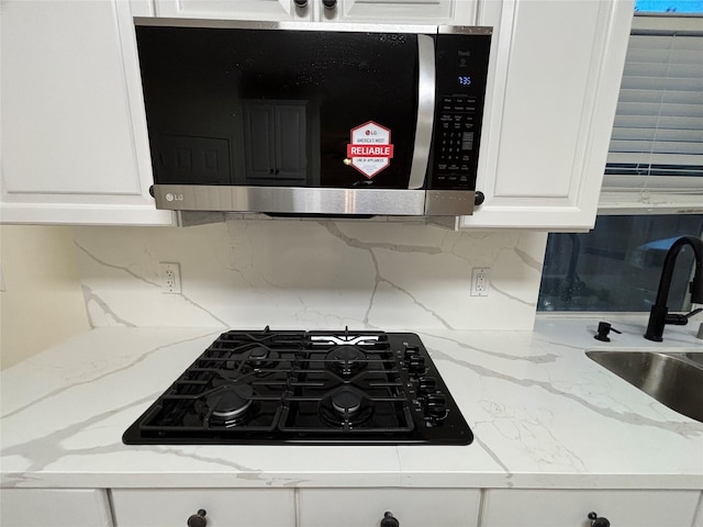 17427 Marigold Dr, Sugar Land, TX 77479 - kitchen view of stainless steel microwave, black gas stovetop, white cabinets, backsplash, and light stone countertops