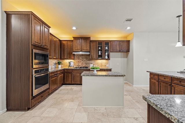 3102 Hillside Landing Trl, Katy, TX 77494 - kitchen featuring appliances with stainless steel finishes, under cabinet range hood, backsplash, light stone countertops, and a kitchen island