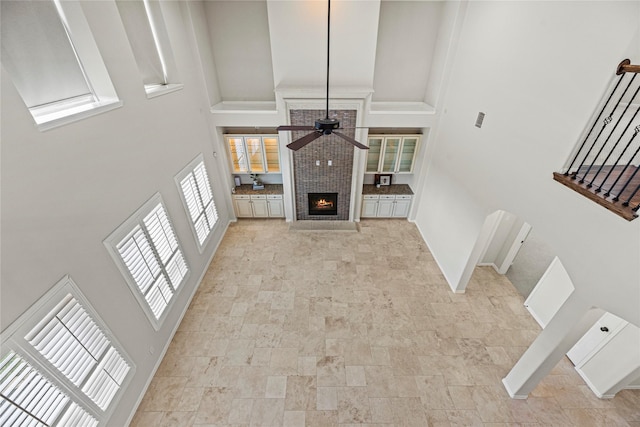 3102 Hillside Landing Trl, Katy, TX 77494 - unfurnished living room featuring a high ceiling, a ceiling fan, a warm lit fireplace, stone finish floors, and stairs