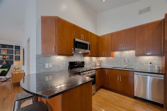308 Dennis St, Houston, TX 77006 - kitchen with stainless steel appliances, a peninsula, brown cabinetry, a kitchen bar, and light wood finished floors