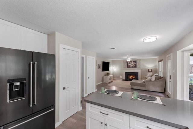 3715 Ember Spring Dr, Kingwood, TX 77339 - kitchen with high quality fridge, light wood finished floors, a brick fireplace, white cabinetry, and dark countertops
