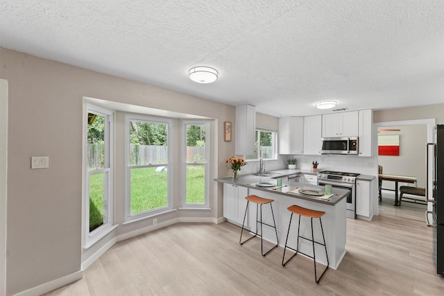 3715 Ember Spring Dr, Kingwood, TX 77339 - kitchen featuring stainless steel appliances, white cabinets, a breakfast bar area, light wood-type flooring, and a textured ceiling