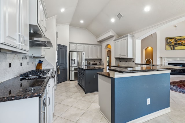 8411 Middle Canyon Rd, Katy, TX 77494 - kitchen with under cabinet range hood, stainless steel appliances, arched walkways, vaulted ceiling, and light tile patterned floors