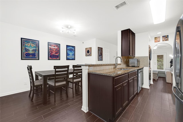 1860 White Oak Dr Unit 251, Houston, TX 77009 - kitchen featuring arched walkways, wood finish floors, dark brown cabinetry, light stone counters, and backsplash