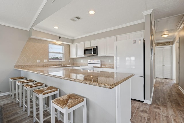 4004 Ector Dr, Galveston, TX 77554 - kitchen featuring white appliances, ornamental molding, a peninsula, wood finished floors, and white cabinetry
