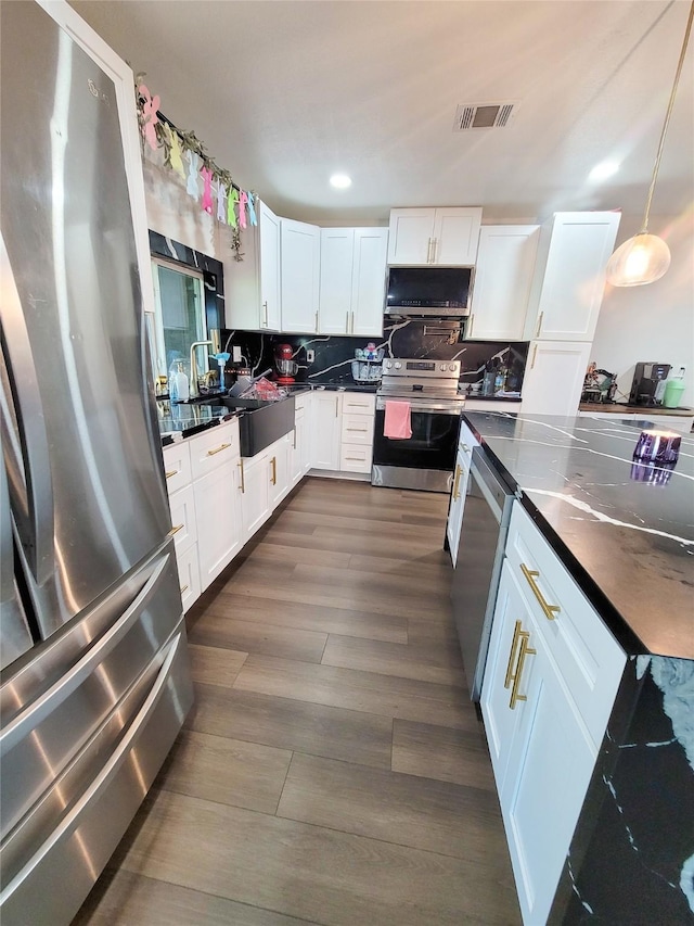 606 E Ahldag St, Wharton, TX 77488 - kitchen with appliances with stainless steel finishes, white cabinets, dark wood-style floors, decorative backsplash, and range hood