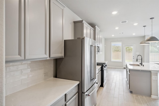 4805 Magnolia Springs Dr, Pearland, TX 77584 - kitchen featuring appliances with stainless steel finishes, decorative backsplash, light wood-type flooring, an island with sink, and pendant lighting