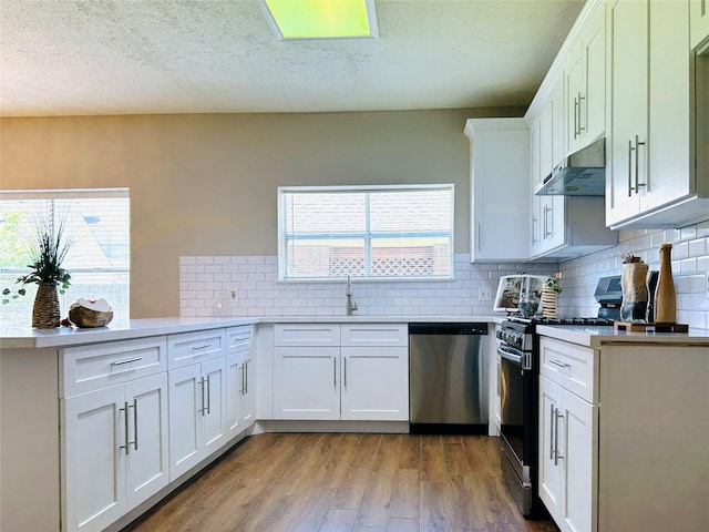 2802 Grants River Cir, Sugar Land, TX 77479 - kitchen with stainless steel dishwasher, black gas range, under cabinet range hood, a peninsula, and light wood-type flooring